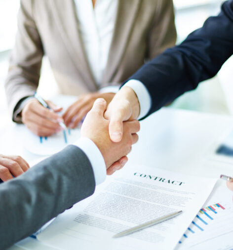 Image of business partners handshaking over business objects on workplace